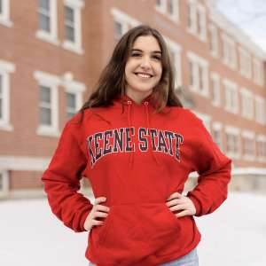 Caroline Catino '26 stands proudly on Fiske Quad in a red Keene State College sweatshirt